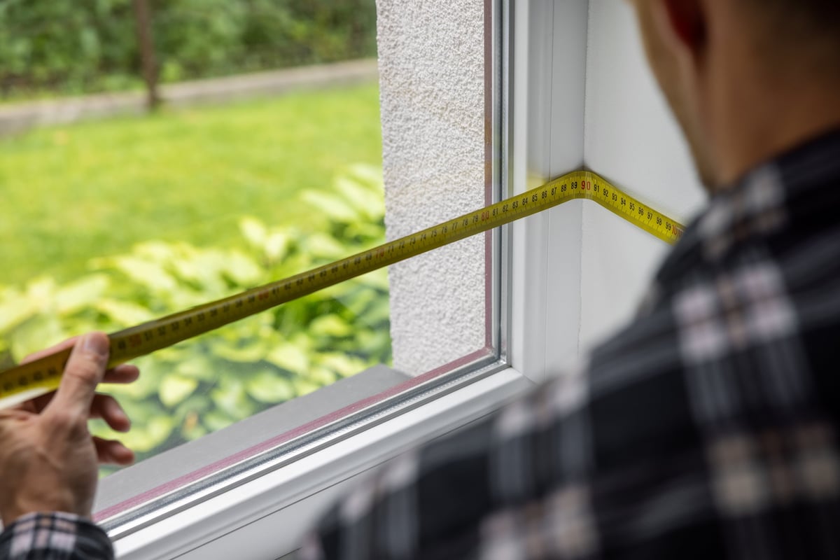 Technician measuring a white replacement window frame